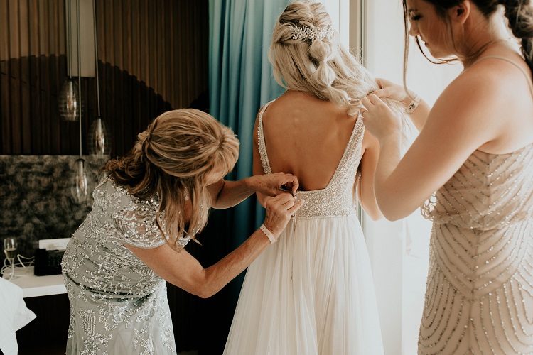 mother helping bride with wedding dress